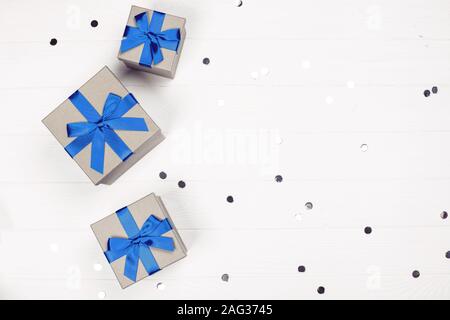 Three present boxes with blue bow on white wooden background with confetti. Flat lay, place for text. Stock Photo
