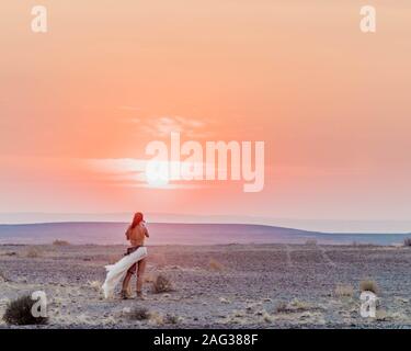 Beautiful shot of a woman admiring the setting sun in the horizon standing in the wild beach Stock Photo