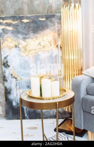 Three unlit white paraffin candles stand on a glass gold bedside table. Expensive interior in shades of gray, gold and blue. Close up. Stock Photo