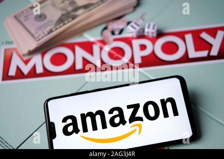 Amazon logo on smartphone placed next to Monopoly game with real money. Conceptual photo. Stock Photo