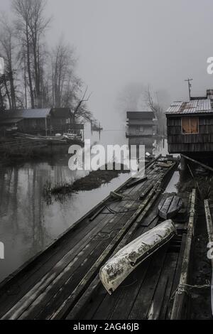 Vertical shot of wooden cabins and pieces of wood on the shore of a lake enveloped in fog Stock Photo