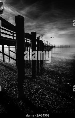 Vertical greyscale shot of a wooden dock with columns on the lake under the beautiful storm clouds Stock Photo
