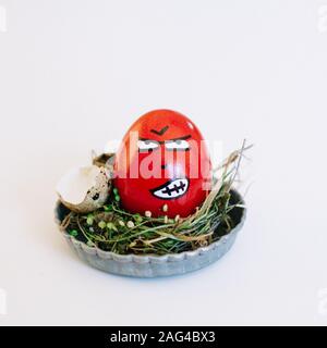 Depiction of an angry face on a red egg in a cute small plate on a white background Stock Photo