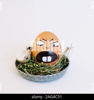 Depiction of an angry face on an egg in a cute small plate on a white background Stock Photo