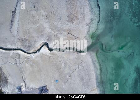 High angle shot of a big crack on the stony shore next to the turquoise water Stock Photo