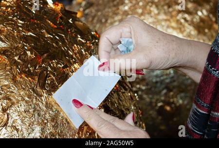 hand of buddhist gilding gold leaflet on golden ball in temple to worship buddha