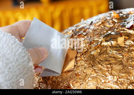 hand of buddhist gilding gold leaflet on golden ball in temple to worship buddha