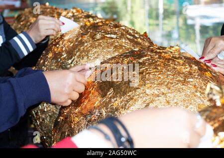 hands of buddhist gilding gold leaflet on golden ball in temple to worship buddha