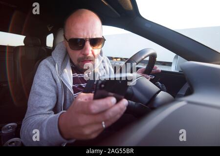 Man driving car using mobile phone texting message or calling. RDriver holding smart phone while driving car on the road. People transportation danger Stock Photo