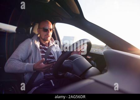 Man looking at mobile phone while driving a car. Stock Photo