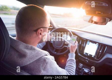 Man looking at mobile phone while driving a car. Stock Photo