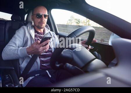 Man looking at mobile phone while driving a car. Stock Photo