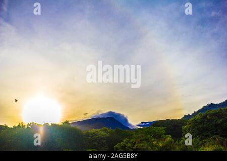 Beautiful shot forested mountains with the sun shining in a blue sky in the background Stock Photo