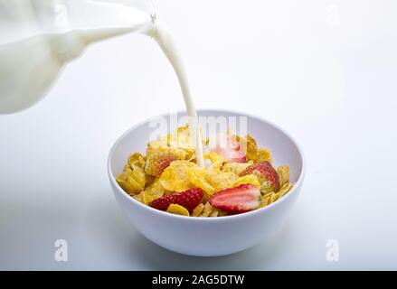 Milk being poured out of a jar into a bowl of cereal and strawberries on a white background Stock Photo
