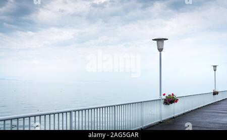 Beautiful view of a pier with white railings and street lamps with the calm sea and the white sky Stock Photo