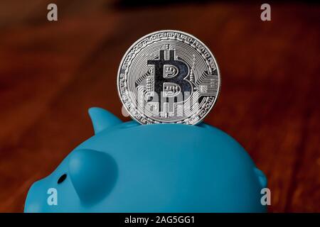 Large Bitcoin being deposited into a piggy bank Stock Photo