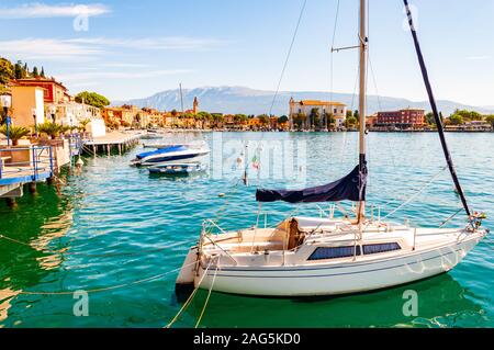 Toscolano Maderno, Lombardy, Italy - September 12, 2019: View on sailing yacht and boats parked on crystal clear blue water of amazing lake Garda and Stock Photo