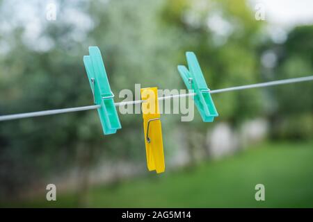Yellow and blue clothespins with blurry green garden background. Sharp close up of those object attached to a wire. Stock Photo