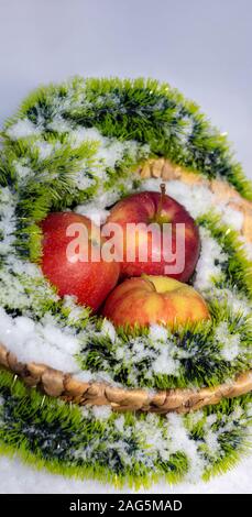 Red apples on the snow in a wicker basket. snow and apples in nature close-up Stock Photo