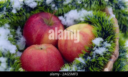 Red apples on the snow in a wicker basket. snow and apples in nature close-up Stock Photo