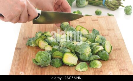 Brussels sprouts. Woman cuts fresh organic Brussels sprouts on a wooden cutting board, close up on white background Stock Photo