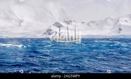 Extreme sailing conditions in Antarctica, as a three masted schooner sails south in a gale, passing the snow-capped mountains and glaciers of the Sout Stock Photo