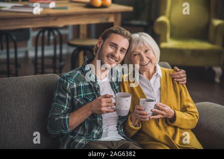 Happy people. Grey-haired elderly woman having tea with son Stock Photo