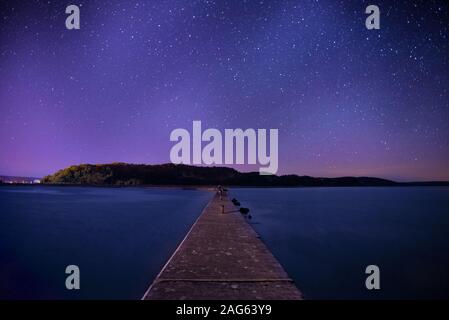 Beautiful shot of a long wooden pier in the center if a lake under the sky full of stars Stock Photo