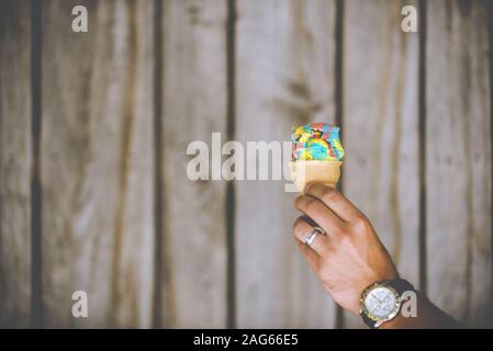 Closeup shot of a male hand holding a colorful ice cream  on a wooden background Stock Photo