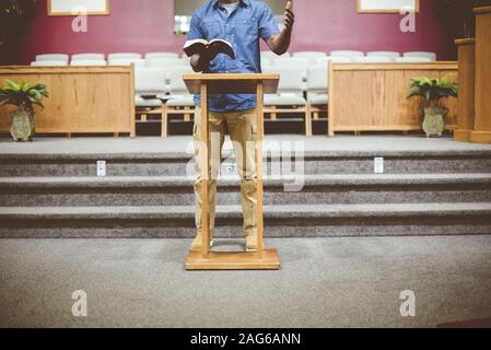 Male standing while reading the bible near a wooden stand with a blurred background Stock Photo