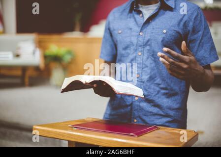 Closeup shot of a male reading the bible near a wooden stand with a blurred background Stock Photo