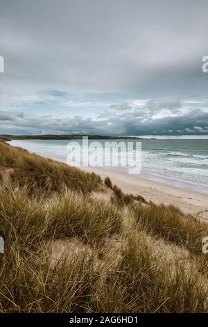 Vertical shot of the grass covered beach by the calm ocean captured in Cornwall, England Stock Photo