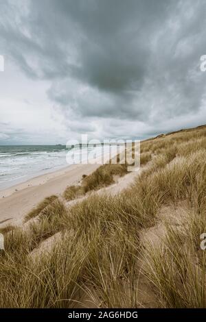 Vertical shot of the grass covered beach by the calm ocean captured in Cornwall, England Stock Photo