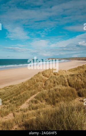 Vertical shot of the grass covered beach by the calm ocean captured in Cornwall, England Stock Photo