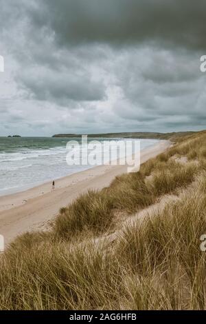 Vertical shot of the grass covered beach by the calm ocean captured in Cornwall, England Stock Photo