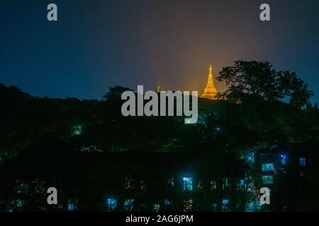 The Shwedagon Pagoda's illuminated golden stupa is visible behind the darkened buildings of Yangon (previously called Rangoon) in Myanmar (Burma) Stock Photo