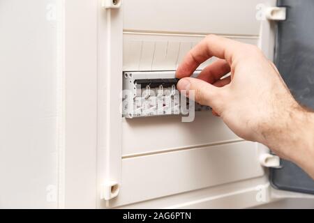 An RCD circuit breaker board with many switches. Man's hand is about switch OFF Stock Photo