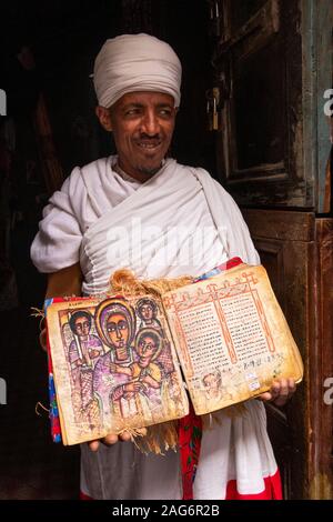 Ethiopia, Amhara, Lalibela, Mount Abuna Yosef, inside, Asheton Maryam Monastery, priest at door holding ancient illuminated gospel on vellum showing n Stock Photo