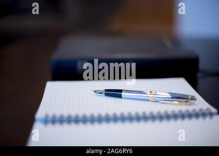 Closeup shot of a fountain pen on a notebook with a blurred bible in the background Stock Photo