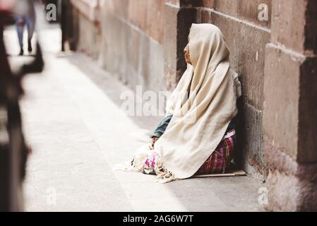 Closeup shot of a homeless elderly sitting on the ground with a blurred background Stock Photo