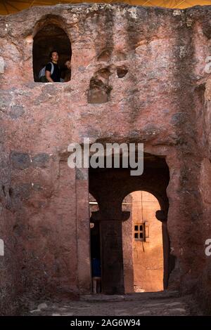 Ethiopia, Amhara Region, Lalibela, visitors inside Bet Danagel chapel looking out of stone window Stock Photo