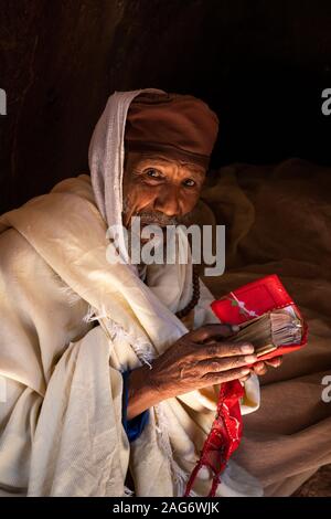 Ethiopia, Amhara Region, Lalibela, Bet Maryam Church, devotee reading gospel in Amharic text looking at camera Stock Photo