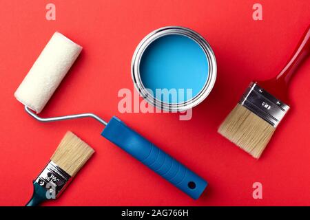 Can of blue paint with brushes and paint roller on red background. Top view. Repair concept. Stock Photo