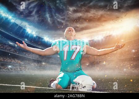 american football player celebrating after scoring a touchdown on the field of big modern stadium with lights and flares at night Stock Photo