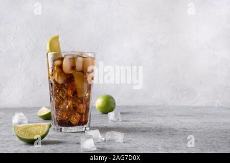 Cocktail Cuba Libre or long island iced tea with rom, cola, lime and ice in glass on grey stone table. Horisontal orientation. Stock Photo