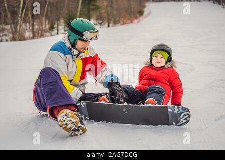 Snowboard instructor teaches a boy to snowboarding. Activities for children in winter. Children's winter sport. Lifestyle Stock Photo