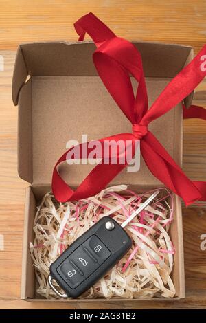 Car key on paper gift box with red ribbon bow and heart on blue table ...
