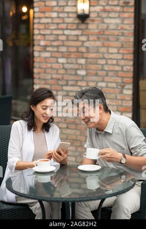 Mature Chinese couple using smartphone in coffee shop Stock Photo