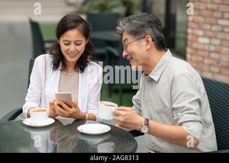 Mature Chinese couple using smartphone in coffee shop Stock Photo