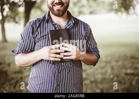 Closeup shot of a male smiling and holding the bible with a blurred background Stock Photo